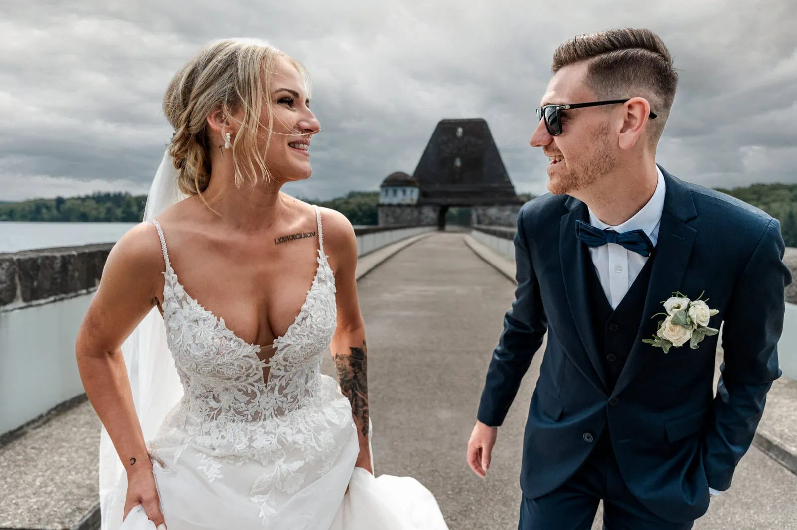 Hochzeitspaar auf einer Brücke mit Schloss im Hintergrund, lachend und verliebt.